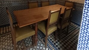 Un coin repas avec une table et des chaises en bois, une horloge murale et un sol carrelé à motifs.
