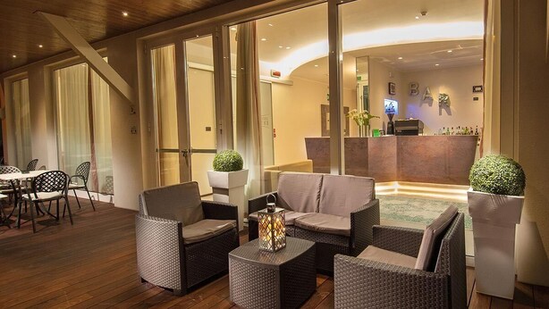 A modern lounge area with wicker furniture, a bar, and a reception desk. - Hotel Ricci (Rimini)