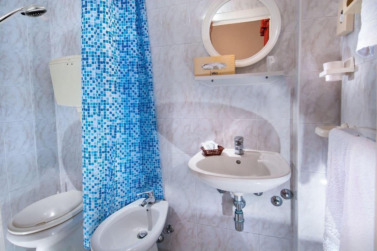 A bathroom with a white toilet, a bidet, a sink, and a shower.