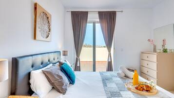 Habitación de hotel con cama, mesita de noche, cómoda y vista al exterior.
