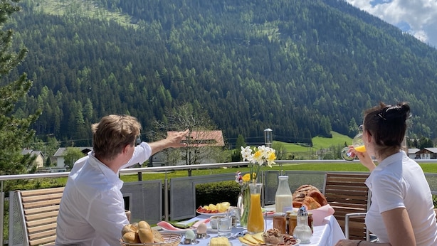 Une table dressée à l’extérieur, avec vue sur la montagne, comprenant des plats et un verre de jus d’orange.