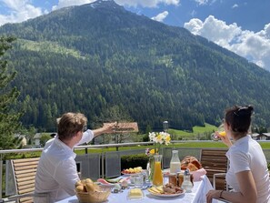 A table set outdoors with a mountain view, including food items and a glass of orange juice. - Apartments Hohenberger (Mallnitz)