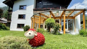 Un bâtiment moderne à deux étages, doté d’une véranda en verre et d’une grande sculpture de mouton rouge en premier plan.
