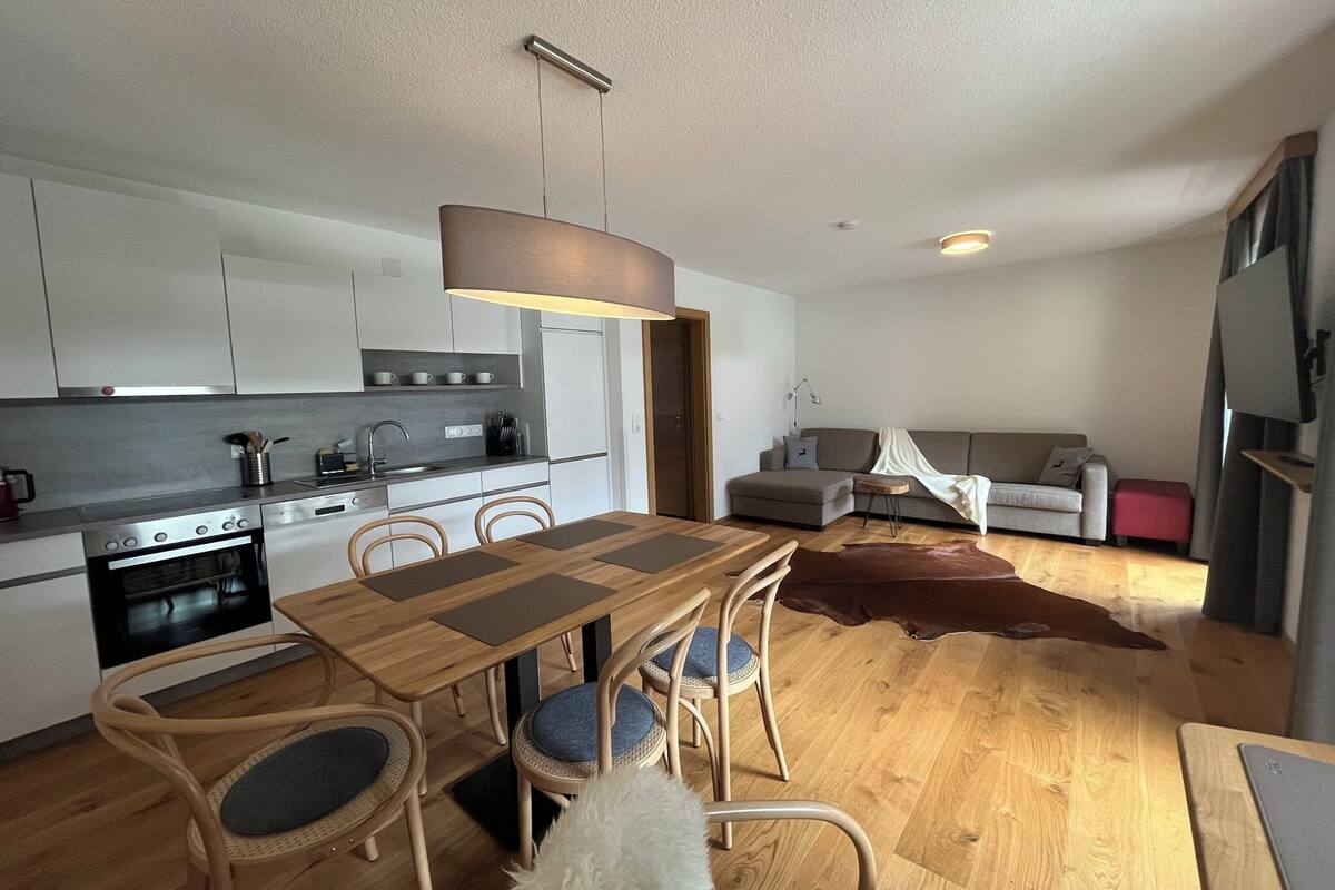 A modern kitchen with a dining area, wooden flooring, and a cozy living space with a sofa and a rug.