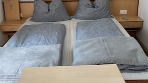 Un lit double avec une literie grise, deux tables de chevet avec des lampes et une tête de lit en bois.
