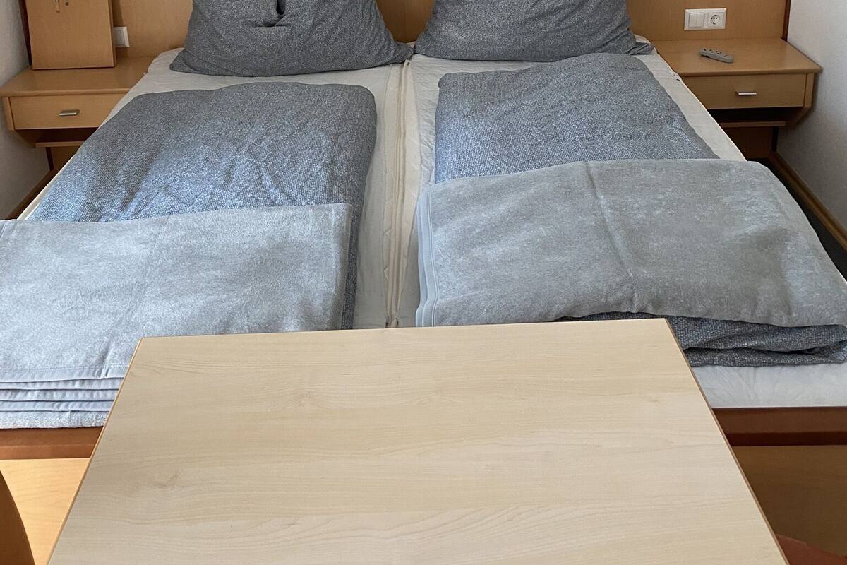 A double bed with grey bedding, two bedside tables with lamps, and a wooden headboard.