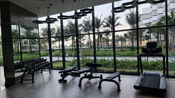 Een sportschool met trainingsapparatuur, grote ramen en uitzicht op palmbomen en gebouwen.