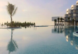 A pool area with clear water, palm trees, and modern buildings in the background.