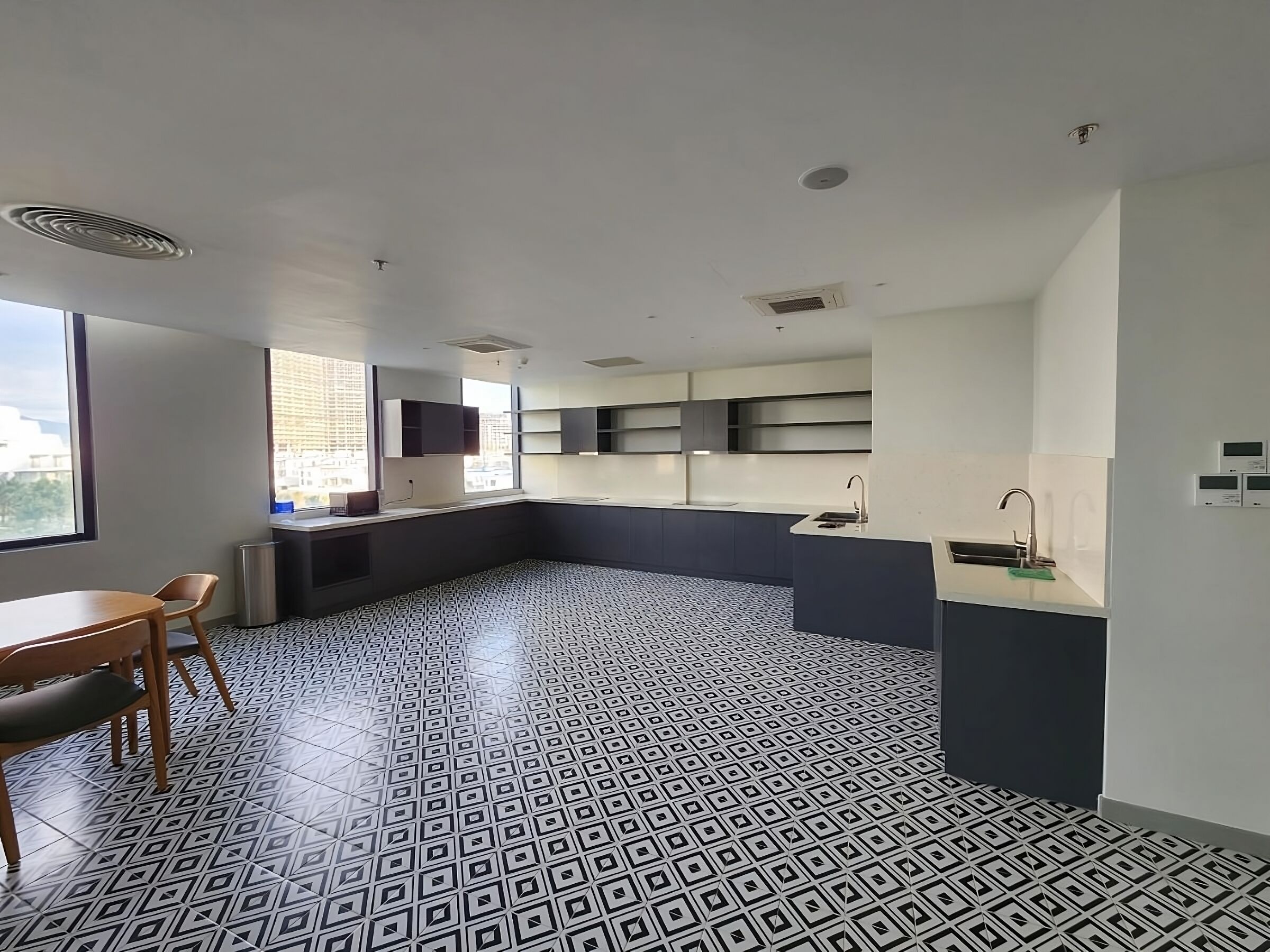 Eine moderne Küche mit dunkler Spritzschutzwand, weißen Arbeitsplatten und einem gemusterten Boden. Ein Essbereich mit Tisch und Stühlen lädt zum Verweilen ein, und ein Fenster bietet Blick auf die Stadt.
