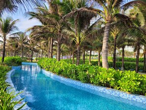 Une piscine bordée de carreaux, entourée d’une végétation luxuriante et de palmiers.