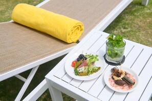 A white outdoor table with a yellow towel, two plates of food, and a glass of drink.
