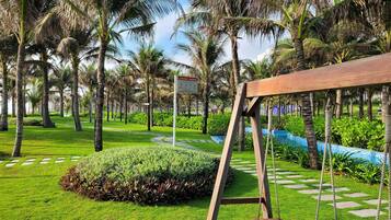 A tropical garden with a wooden swing, palm trees, and a sign.