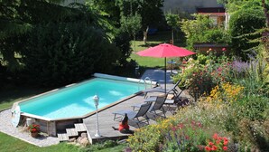 Une piscine rectangulaire dotée d’une terrasse en bois, entourée d’une végétation luxuriante et de fleurs aux couleurs vives.