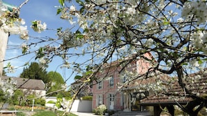Un bâtiment à la façade de style traditionnel, entouré d’arbres en fleurs et d’un jardin bien entretenu.