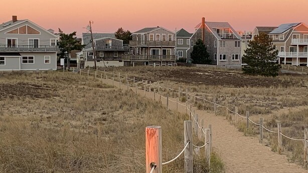 Un sendero arenoso que conduce a una hilera de casas de playa con una valla de madera.