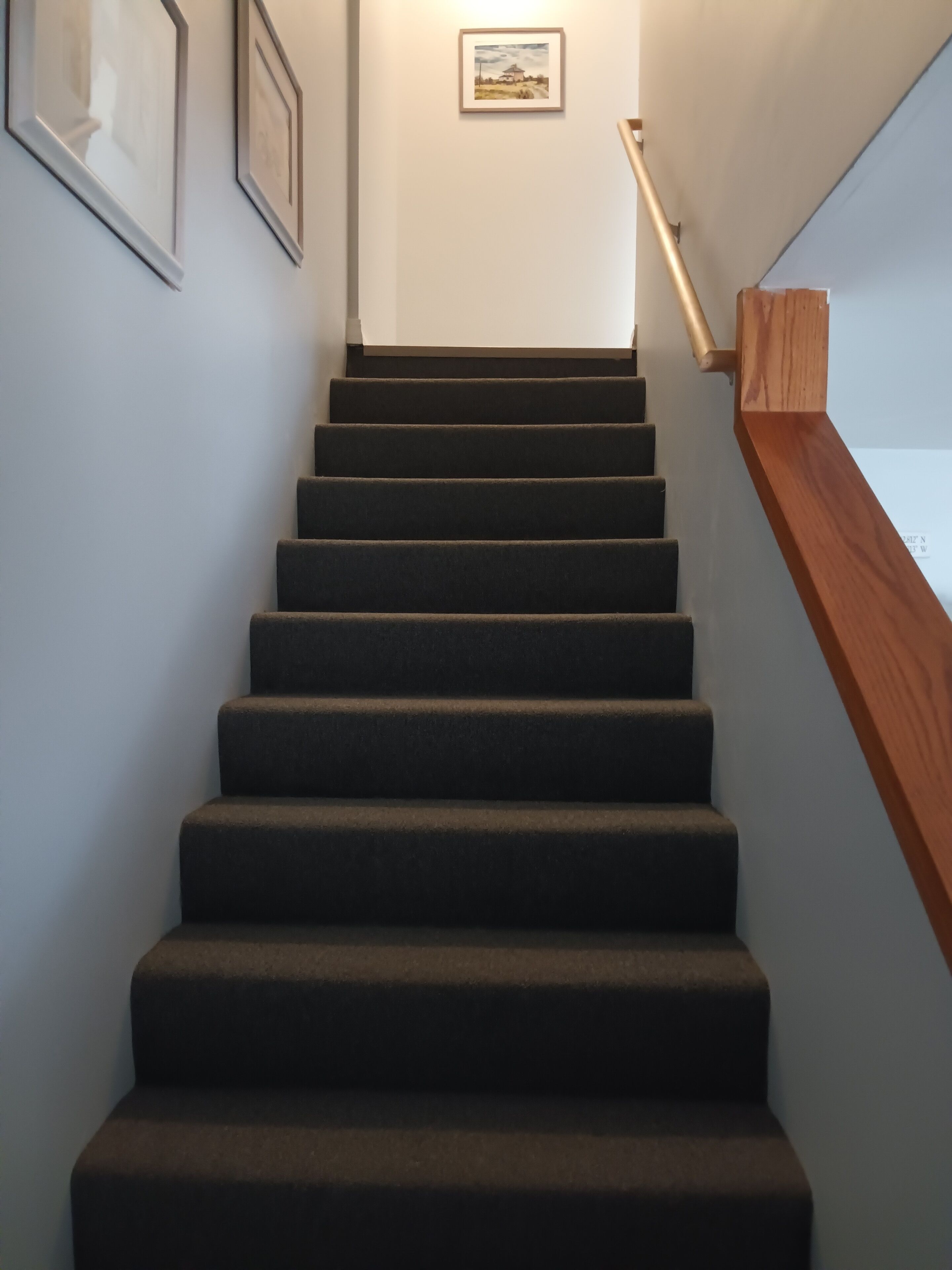 Una escalera alfombrada con barandilla de madera y un cuadro enmarcado en la pared.