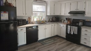 Una cocina con armarios blancos, un refrigerador negro, lavavajillas y estufa.