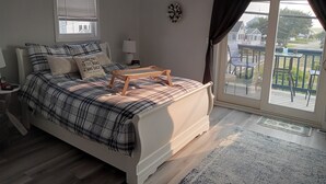 Un dormitorio con cama, una mesita de noche, una lámpara, un reloj y vistas al balcón exterior.