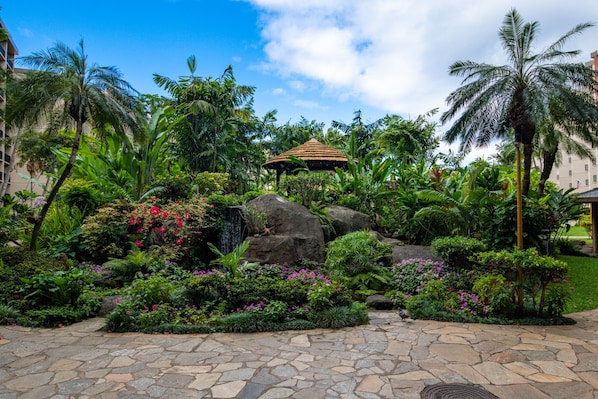 Un jardin tropical avec un sentier en pierre, un kiosque et une végétation luxuriante.