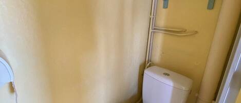 A small, narrow bathroom with a white toilet, a blue shelf above it, and a white wall.