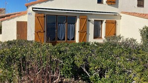 Un edificio de dos pisos con fachada color crema, contraventanas de madera en las ventanas y un balcón pequeño.