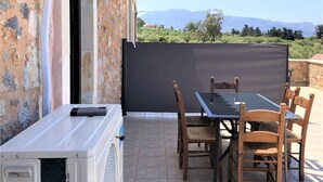 A patio with a table and chairs, a white air conditioning unit, and a view of mountains. - Ιndependent stone apartment with attic. (Παλαιλώνι βαμου)