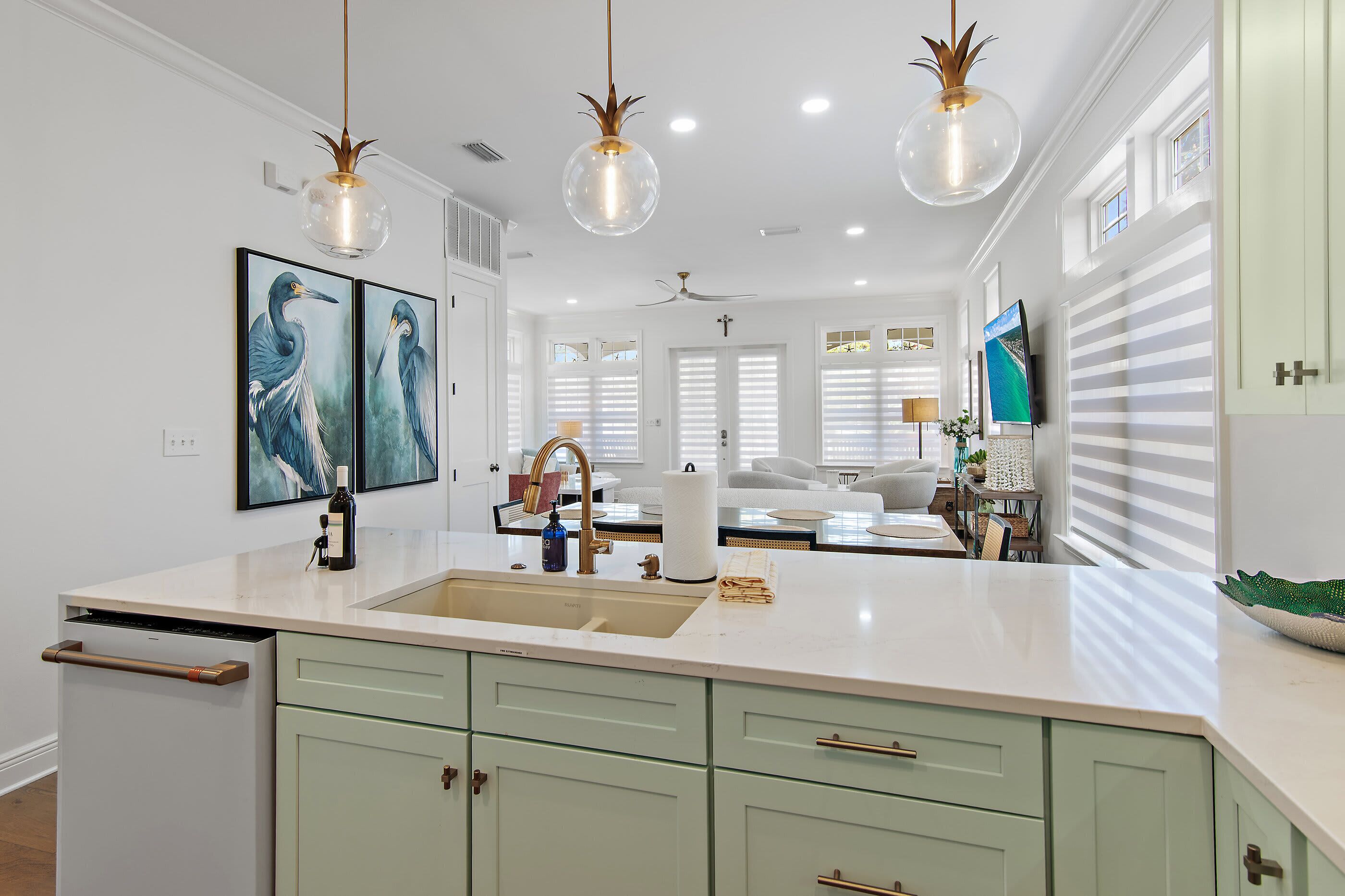 A modern kitchen with a central island, pendant lights, and a dining area with a sofa and table.