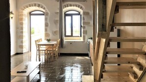 Ein Zimmer mit einer Holztreppe, einem Essbereich mit Tisch und Stühlen sowie zwei Bogenfenstern mit Vorhängen.