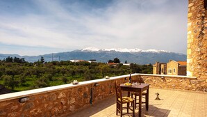 Eine Terrasse mit Steinmauer, einem Tisch mit Stühlen und Blick auf ferne, schneebedeckte Berge.