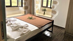 Ein Schlafzimmer mit Bett, Fenster, Steinwand und einem kleinen Tisch mit Pflanze.
