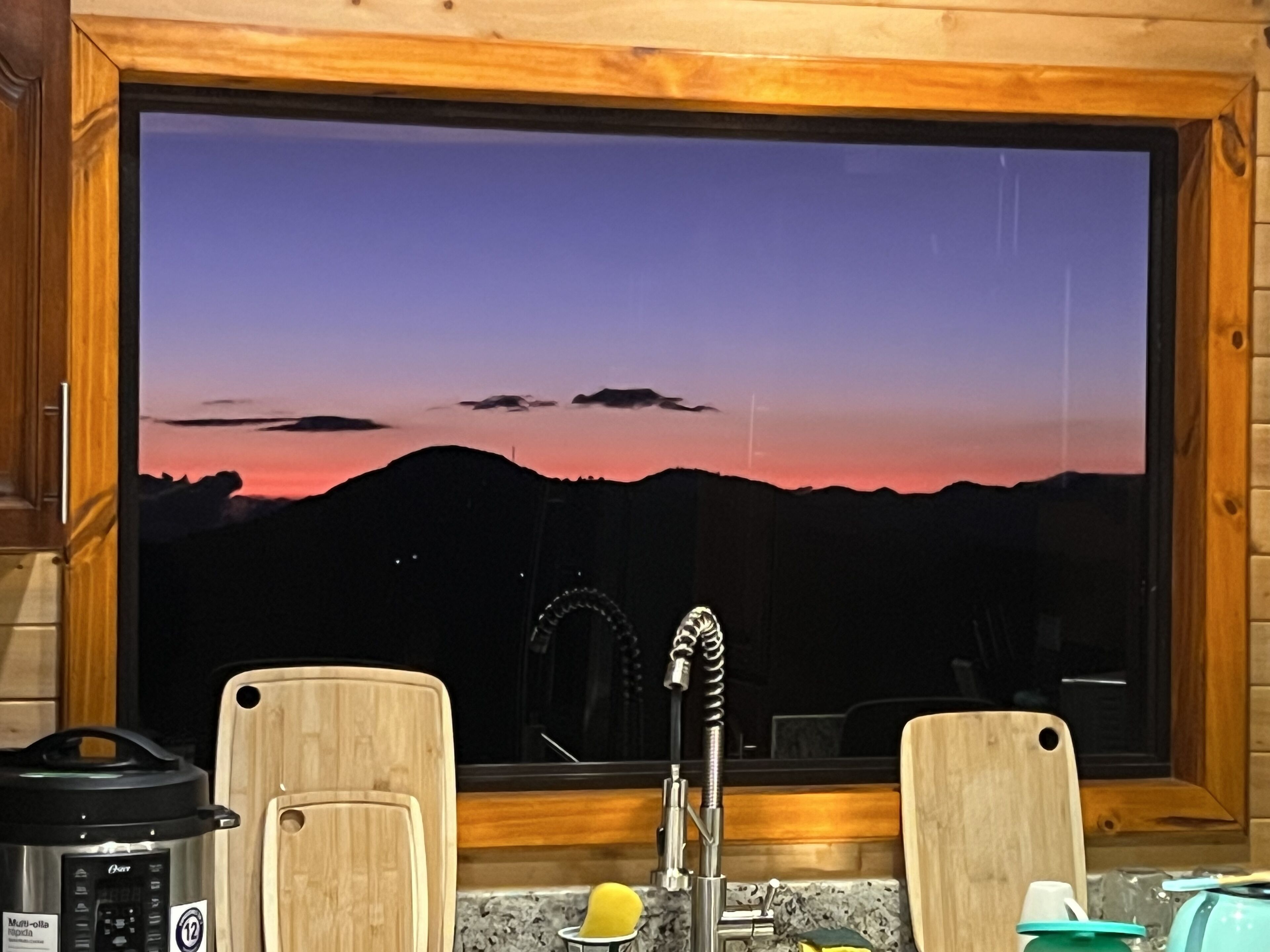 Une cuisine dotée d’une grande fenêtre offrant une vue imprenable sur les montagnes au coucher du soleil.