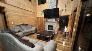 A log cabin interior with a stone fireplace, a large flat-screen TV, and a cozy seating area with a sofa and ottoman. - Full house with breathtaking views (San José)