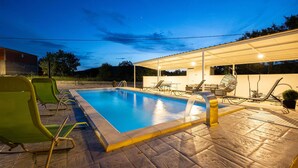 En swimmingpool med liggestole og et overdækket siddeområde.