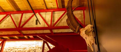 Une trompe de chasse fixée au mur d’une pièce dont le plafond est en bois et qui présente des poutres rouges apparentes.
