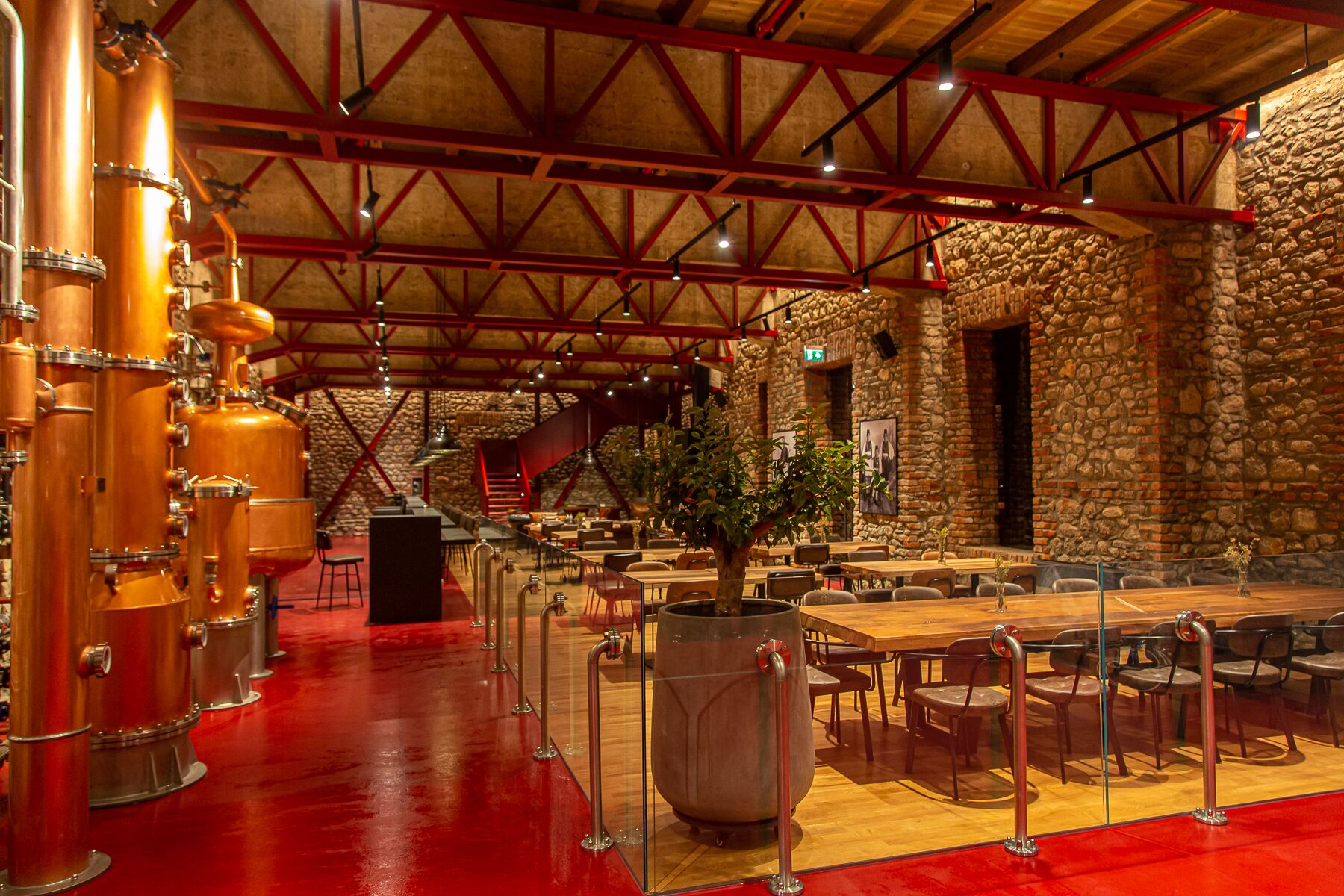 A spacious restaurant with high ceilings, exposed beams, and a stone wall. There are multiple tables and chairs arranged for dining.