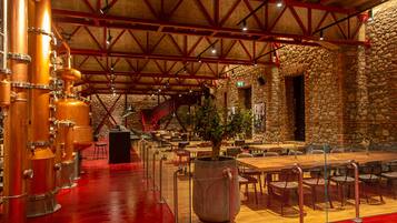 A spacious restaurant with high ceilings, exposed beams, and a stone wall. There are multiple tables and chairs arranged for dining.
