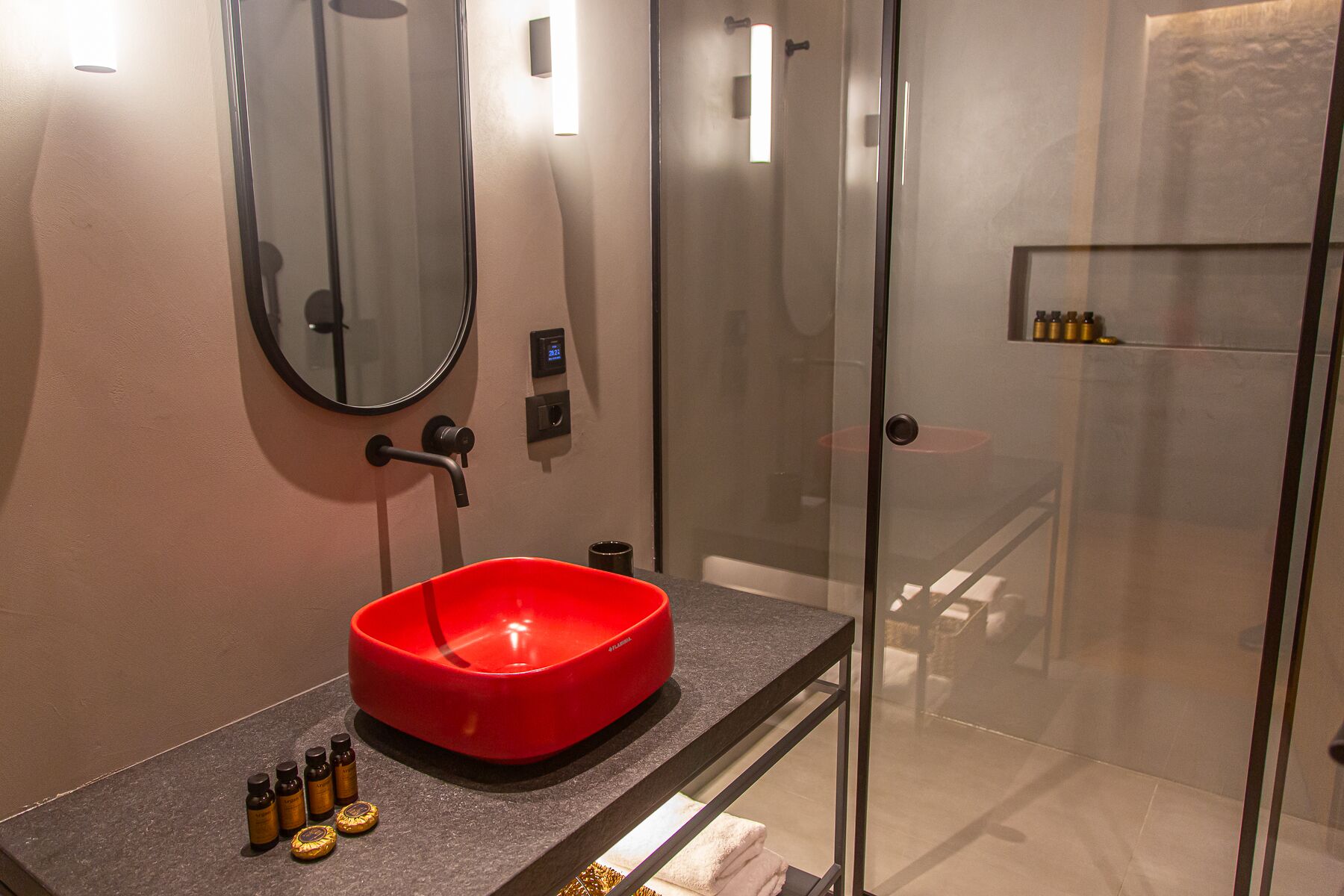 A modern bathroom with a glass shower enclosure, a red basin, and a mirror.