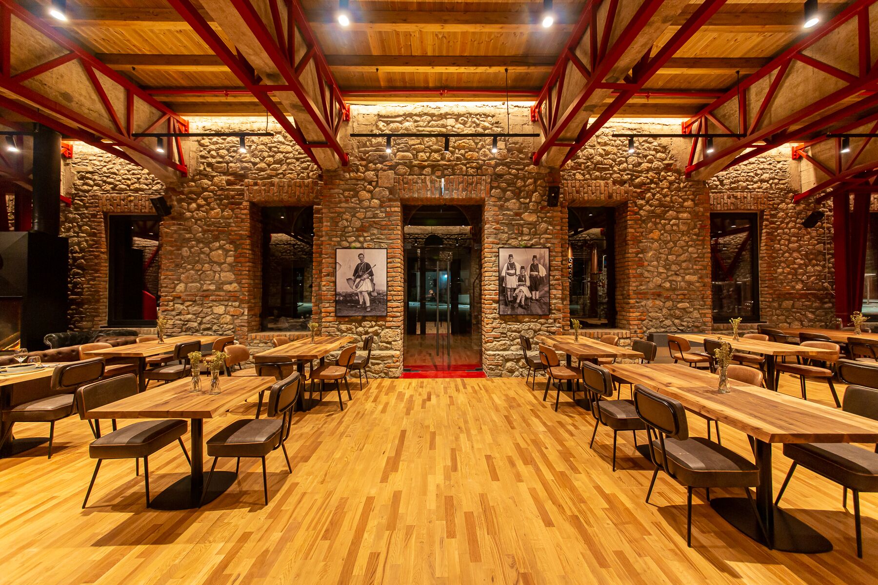 A spacious dining area with wooden tables and chairs, stone walls, and a high ceiling with exposed beams.