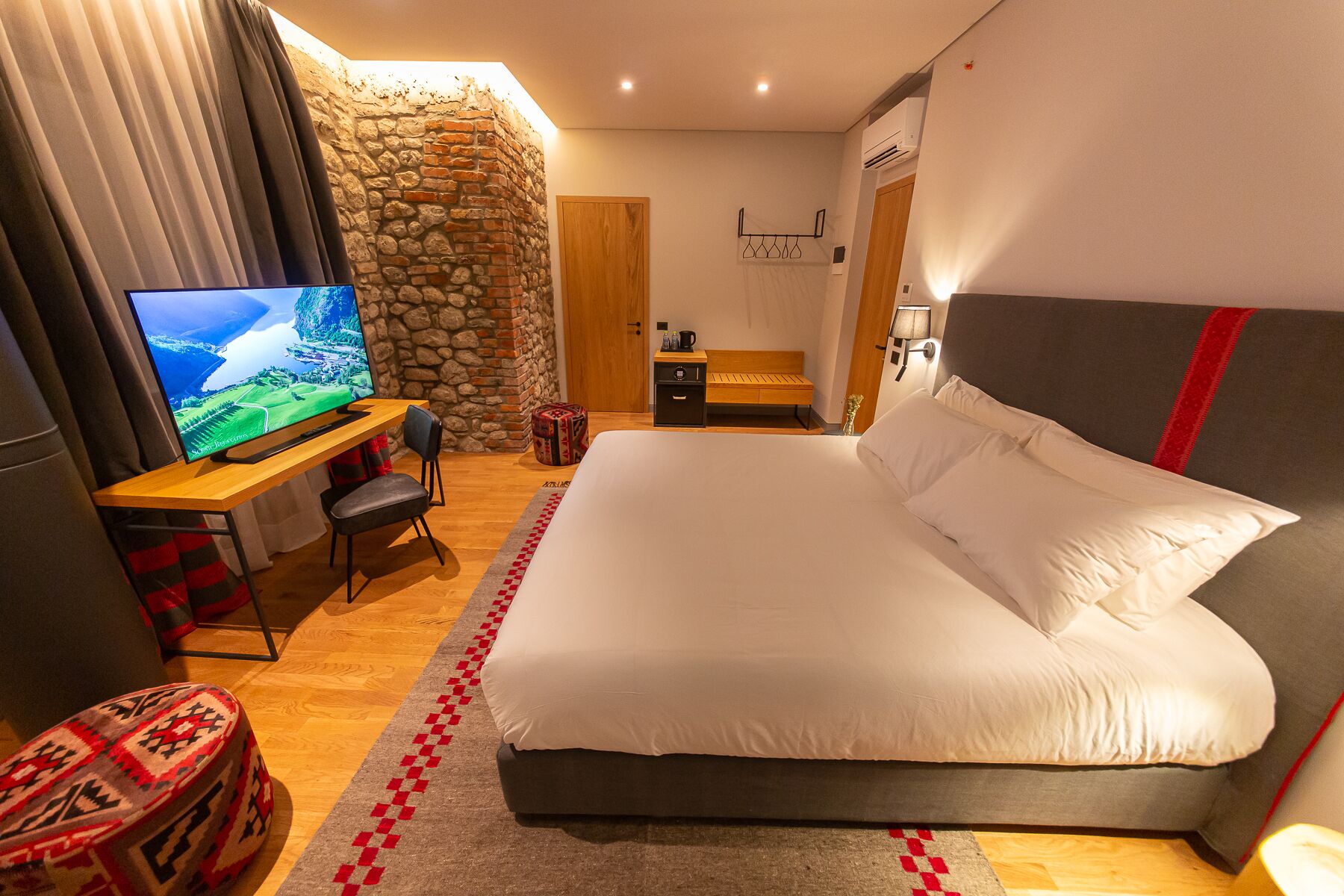 Un dormitorio con una cama grande, un televisor sobre un escritorio de madera, una pared de piedra y una puerta de madera.