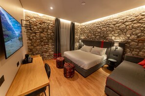 A modern bedroom with a stone wall, a bed, a desk, and a TV. - Melesin Distillery (Leskovik)