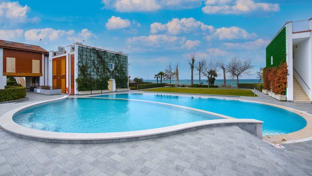 Une piscine à bord incurvé, entourée d’une zone pavée et bordée de bâtiments adjacents.
