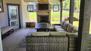 A covered outdoor seating area with a stone fireplace, wicker furniture, and a view of a grassy yard. - Quiet lake getaway offering R&R with 2 electric bikes and optional sunset cruise (Sherrills Ford)