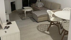 A compact living space with a sofa, a small round table, and a dining table with chairs. There is a ceiling fan, a wall-mounted air conditioning unit, and a hanging light fixture. - Apartment center Albufeira (Albufeira)