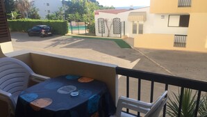 A balcony with a table and chairs, a view of a street with a car and buildings, and a fence with a gate. - Apartment center Albufeira (Albufeira)