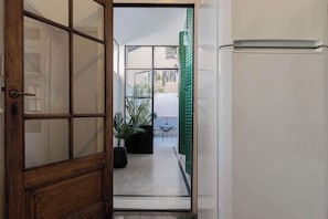A corridor with a wooden door, a white refrigerator, a potted plant, and a table with chairs.