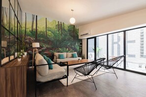 A modern living room with a sofa, chairs, a wooden table, and a large mural of a forest.
