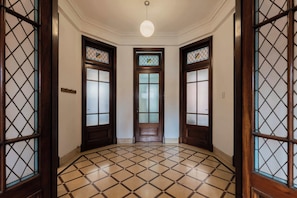 A hallway with a tiled floor, three wooden doors with glass panels, and a hanging light fixture.