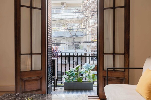 A room with a bed, a window with a view of a balcony, and a potted plant on the windowsill.