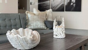 Een moderne woonkamer met een grijze bank, een decoratieve witte keramieken schaal en een glazen vaas op een houten tafel.