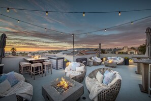 A rooftop patio with outdoor seating, string lights, and a fire feature.